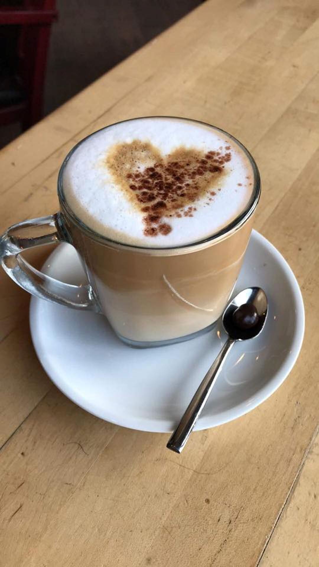 Coffee latte with a heart made in cocoa stencil on a white milk froth.