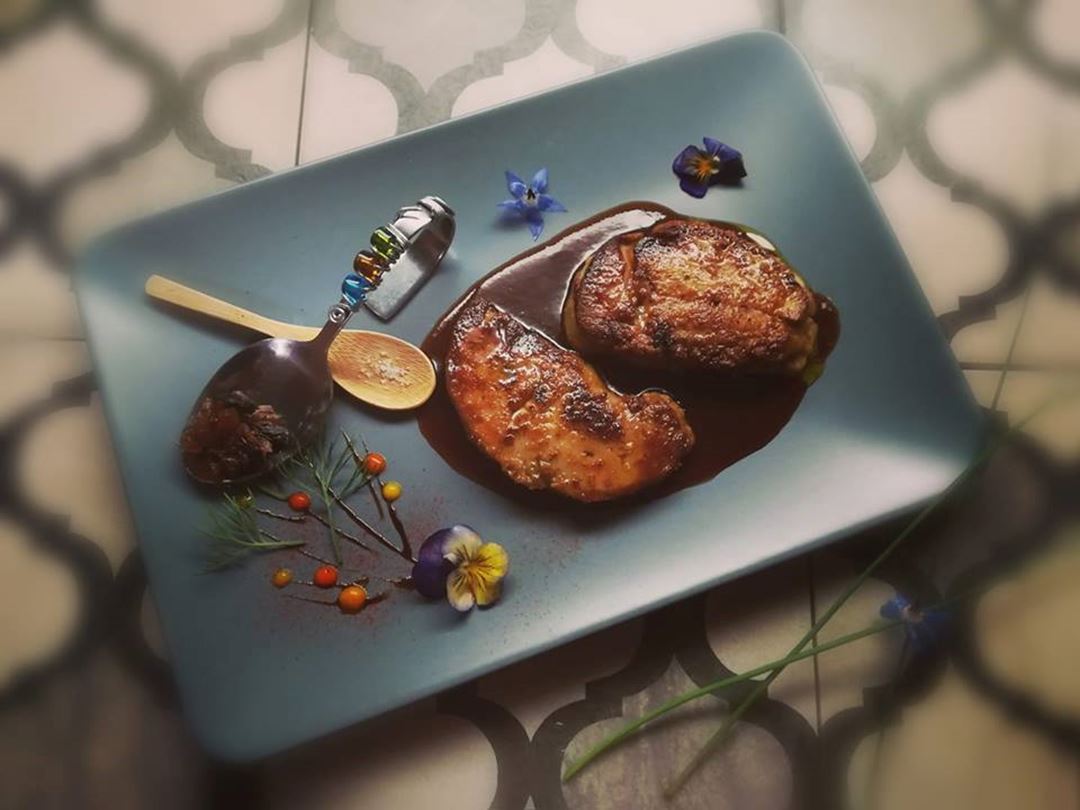 Meat served in a black rectangular plate and accompanied by a drizzle of sauce.